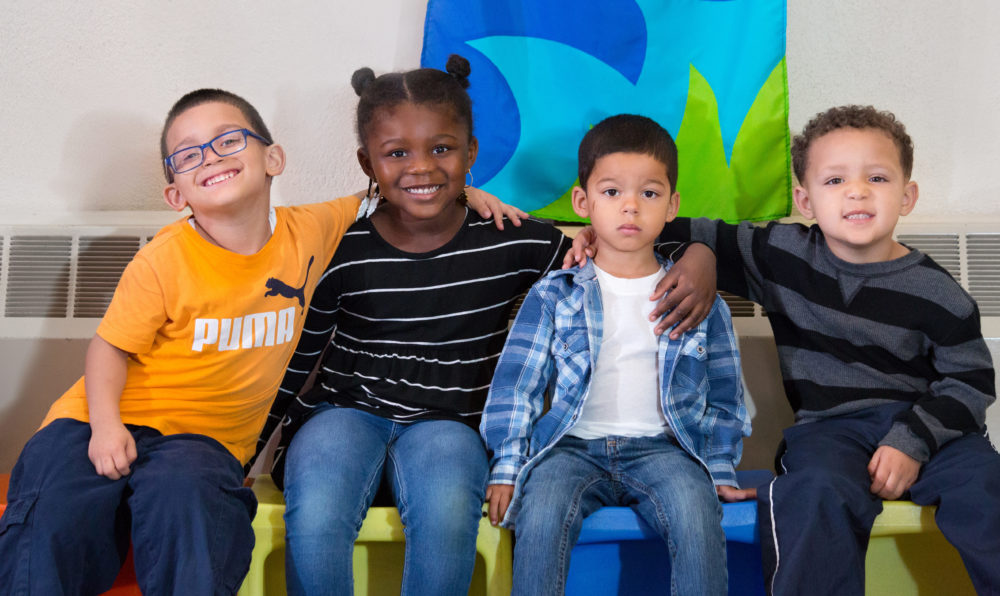 Group photo of four children in early learning center, sitting and smiling at the camera