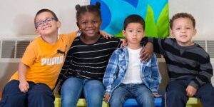 Group photo of four children in early learning center, sitting and smiling at the camera